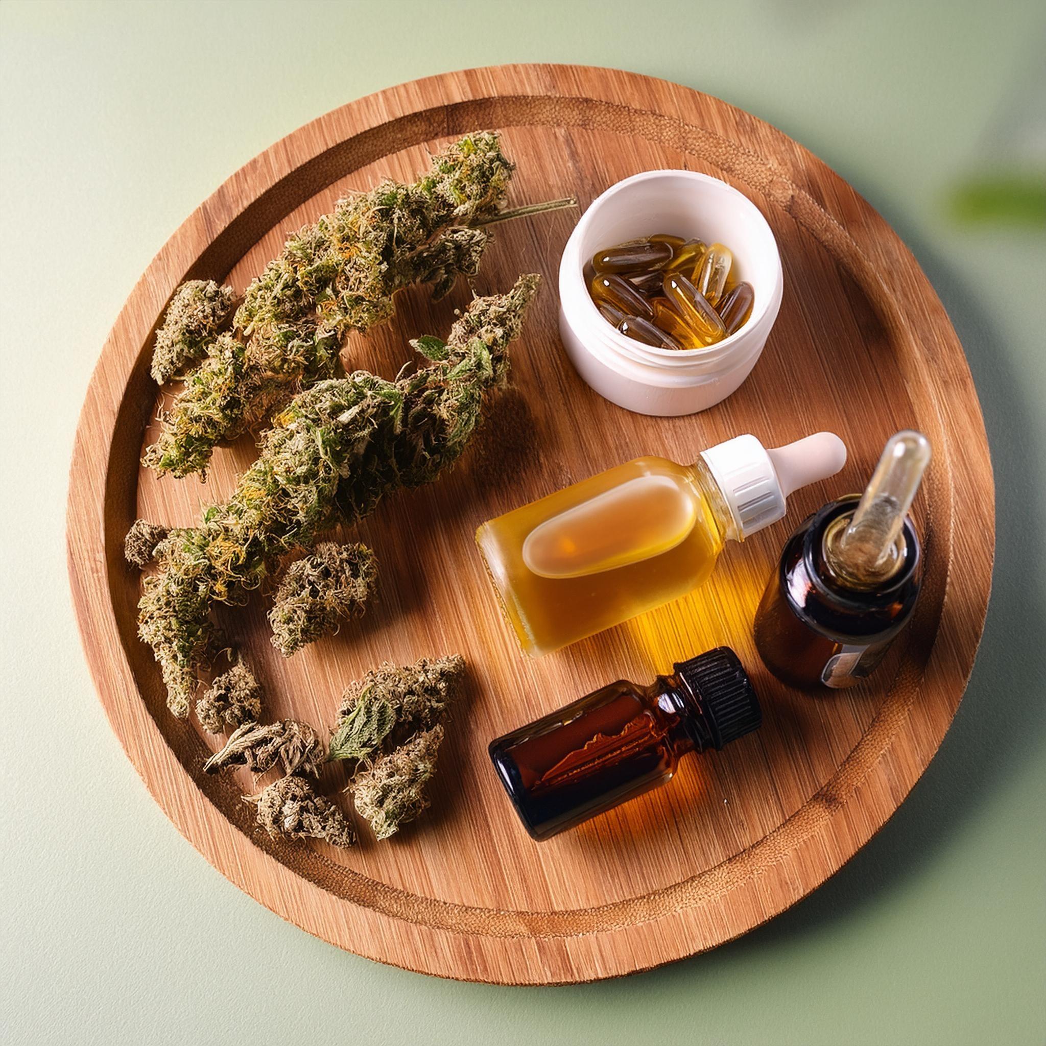 Assorted cannabis buds, CBD oil tinctures, and capsules on a wooden tray for wellness use